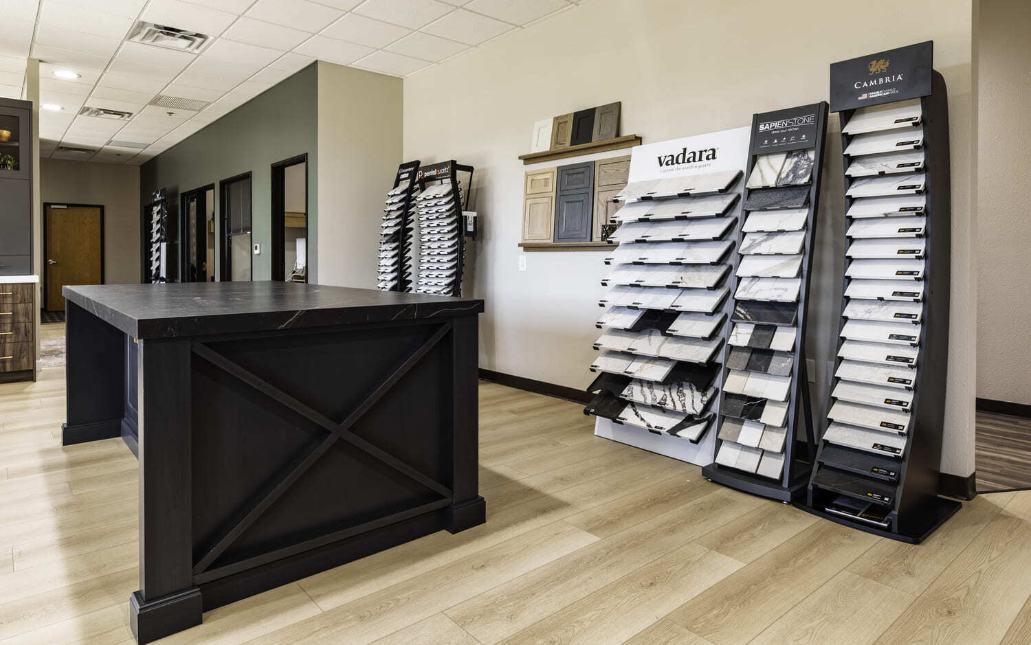 Design showroom with black island, wood floors, and countertop sample racks along a bright wall.