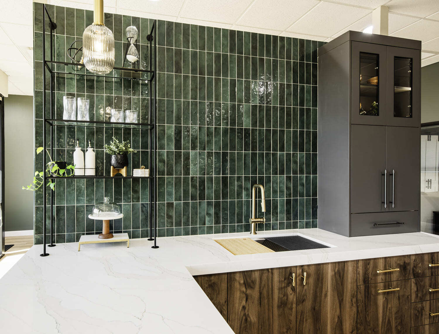 Kitchen showroom with green tile backsplash, white counters, dark cabinets, open shelving, and brass faucet.