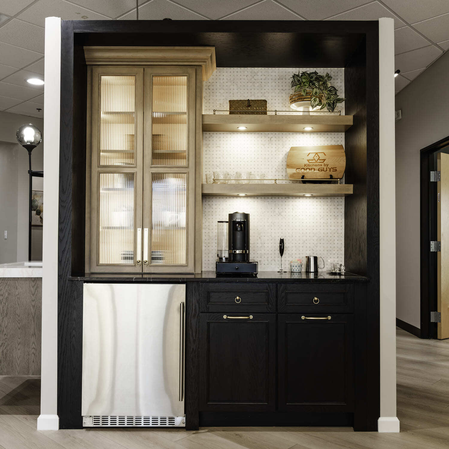 Showroom beverage station with black cabinets, glass-front upper cabinet, open shelves, and stainless fridge.