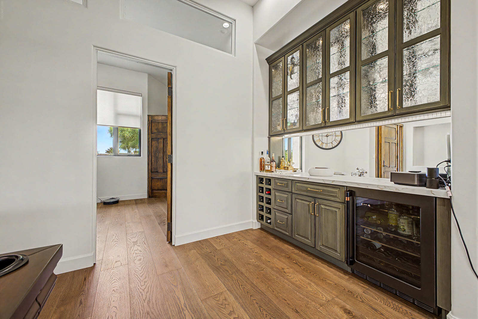 Built-in bar with glass cabinets, wine fridge, brass hardware, and warm wood flooring.